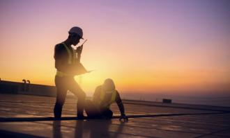 Two technicians service yearly preventive maintenance solar cells on roof factory under morning sunlight