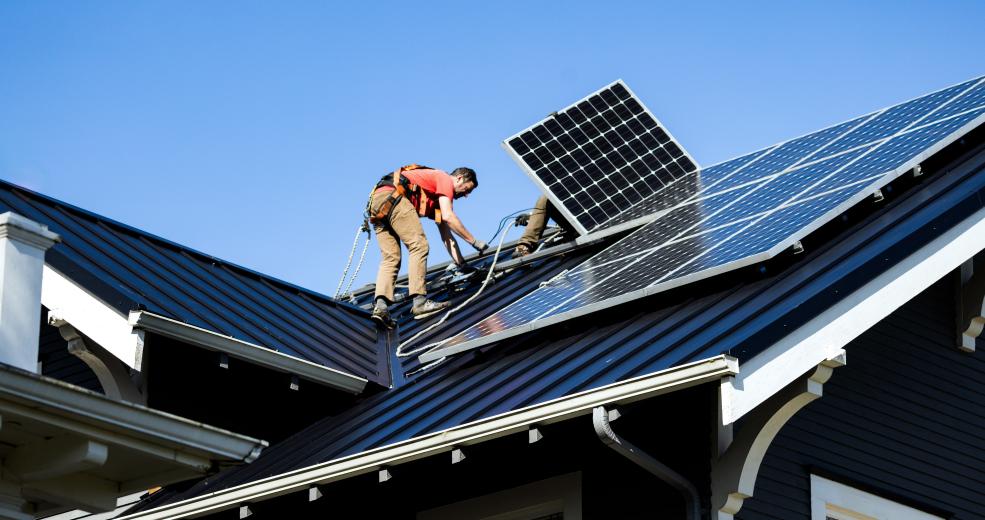 worker installing solar panels on house